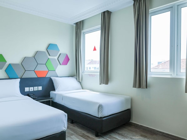 A hotel room with two beds, a nightstand, a wall-mounted light, and a window with curtains. - ibis budget Singapore Jasmine (Singapore)