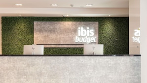 A reception desk with a green wall and a large sign that reads 'ibis budget.'
