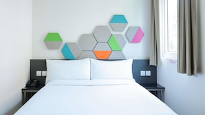 A hotel room with a bed, a nightstand, a phone, and a wall-mounted geometric art piece.