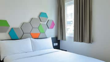 A hotel room with a bed, a wall-mounted geometric art piece, a window with curtains, and a nightstand.