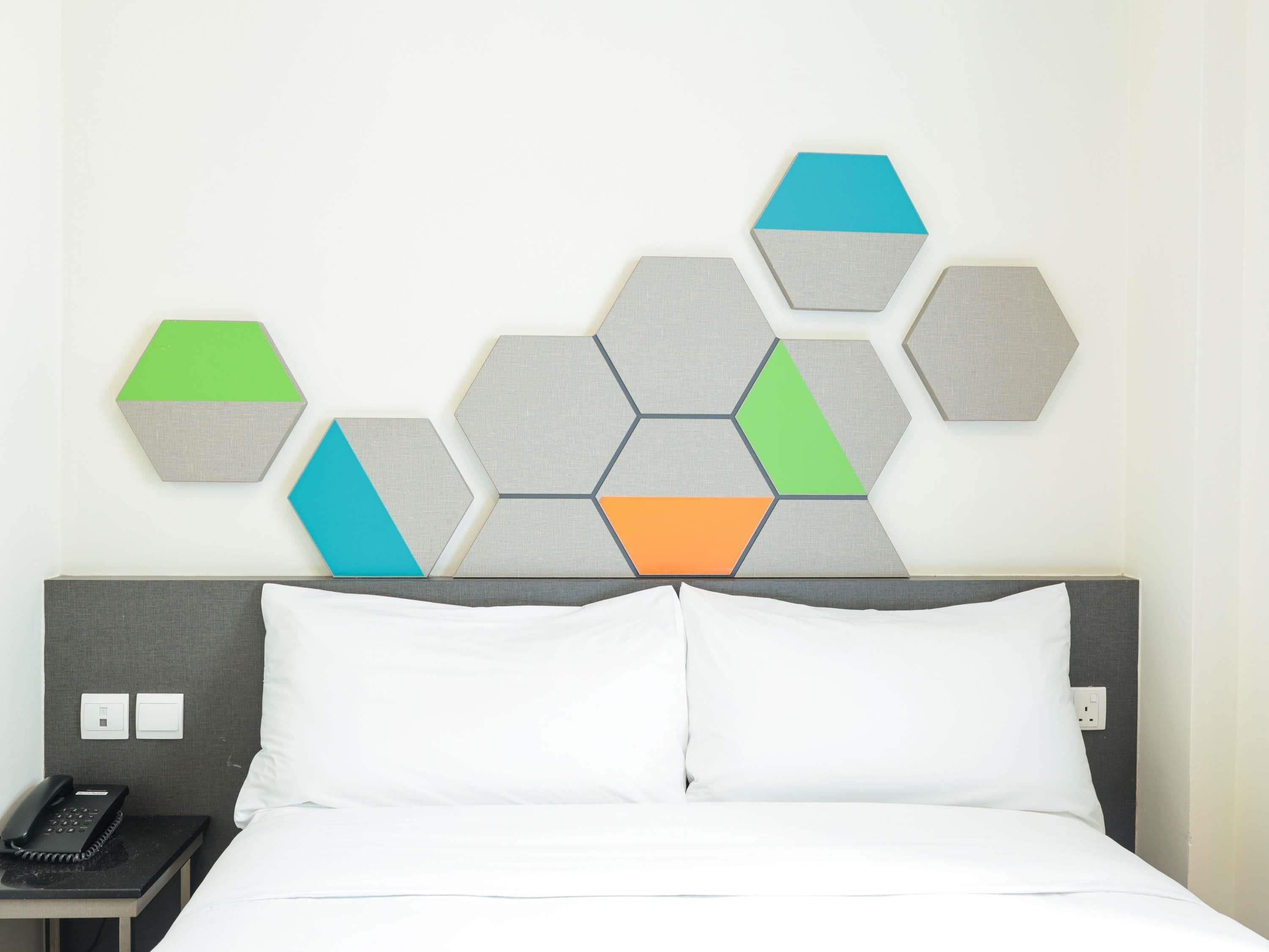 A hotel room with a bed, a nightstand, a phone, and a wall with hexagonal wall art.