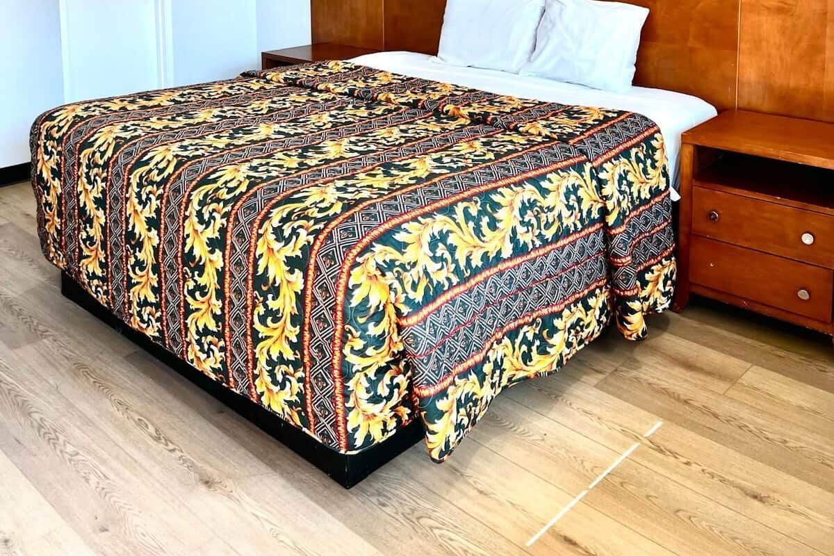 A bedroom with a large bed, a wooden headboard, a nightstand, and a white door.