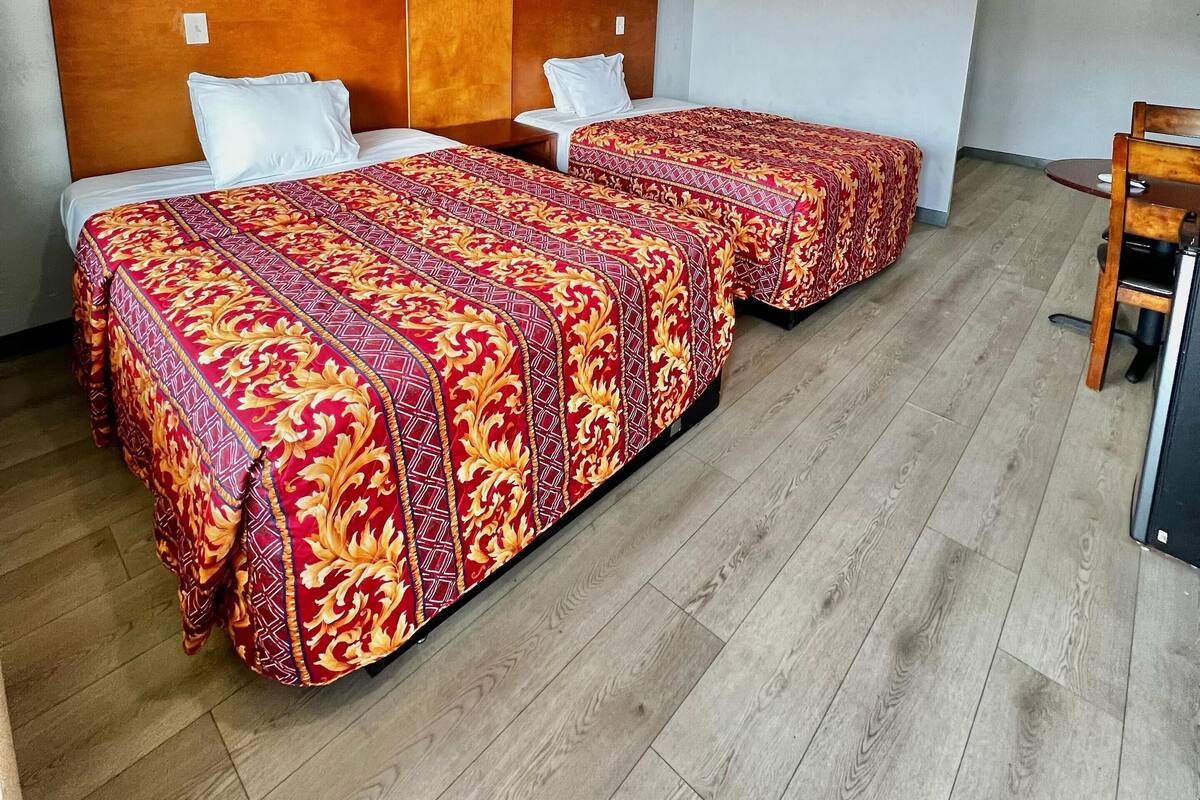 A hotel room with two beds, a wooden headboard, and a small table.