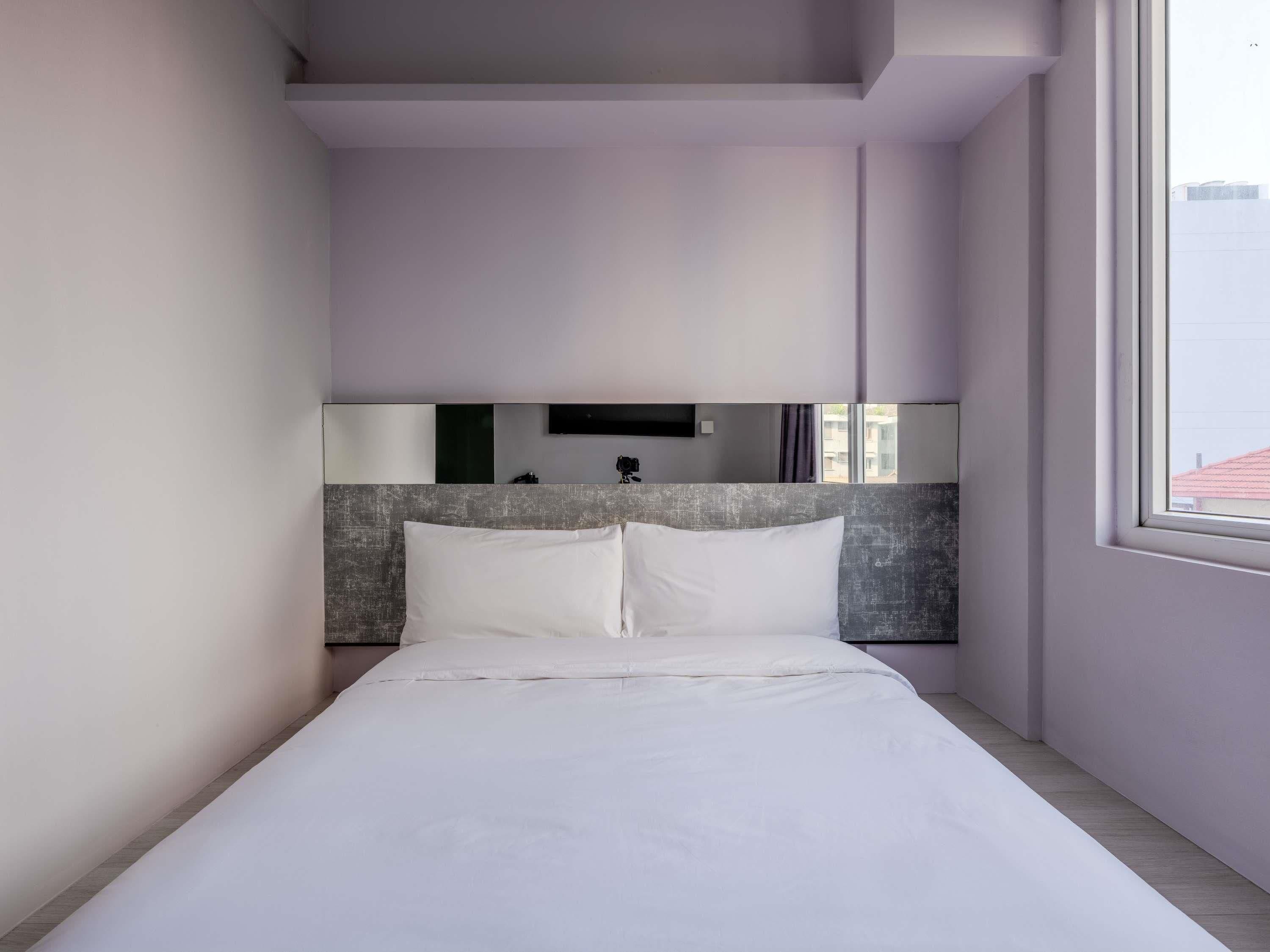 A modern hotel room with a large bed, a flat-screen TV mounted on the wall, and a window providing a view of the outside.