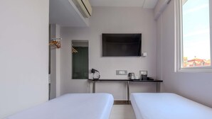 Habitación de hotel con dos camas individuales, un escritorio con televisor de pantalla plana, cafetera y una ventana pequeña.