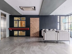 Een modern interieur met een receptiebalie, een houten deur en een zithoek met grijze banken.