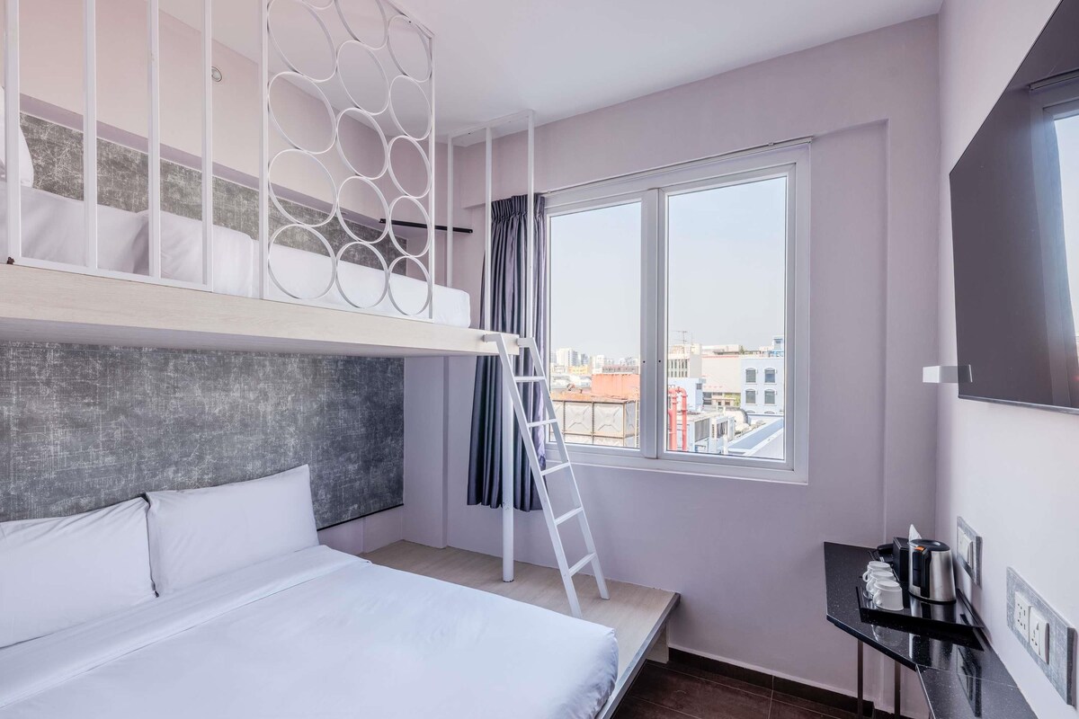 Een moderne hotelkamer met een stapelbed, een bureau, een raam met uitzicht op de stad, en een flatscreen televisie.