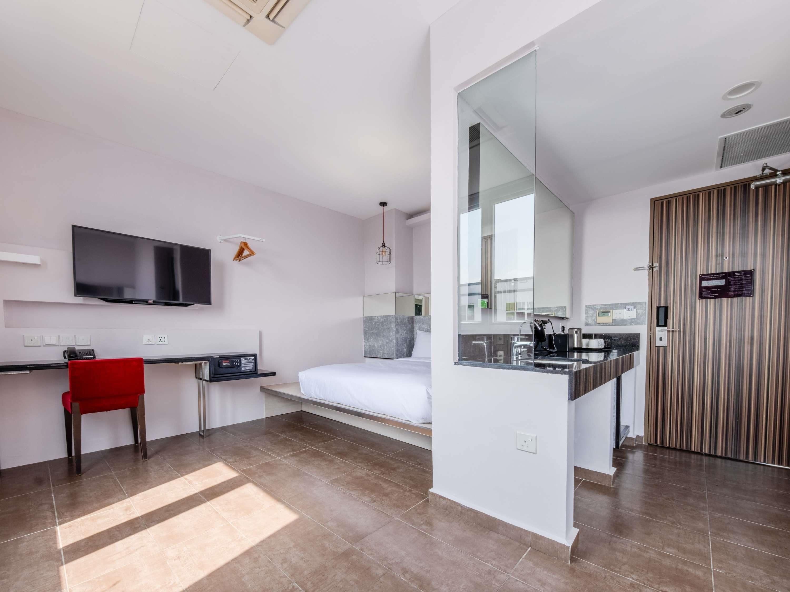 Une chambre d’hôtel moderne équipée d’un lit, d’un bureau, d’une télévision, d’un fauteuil rouge et d’une salle de bain avec un miroir et un lavabo.
