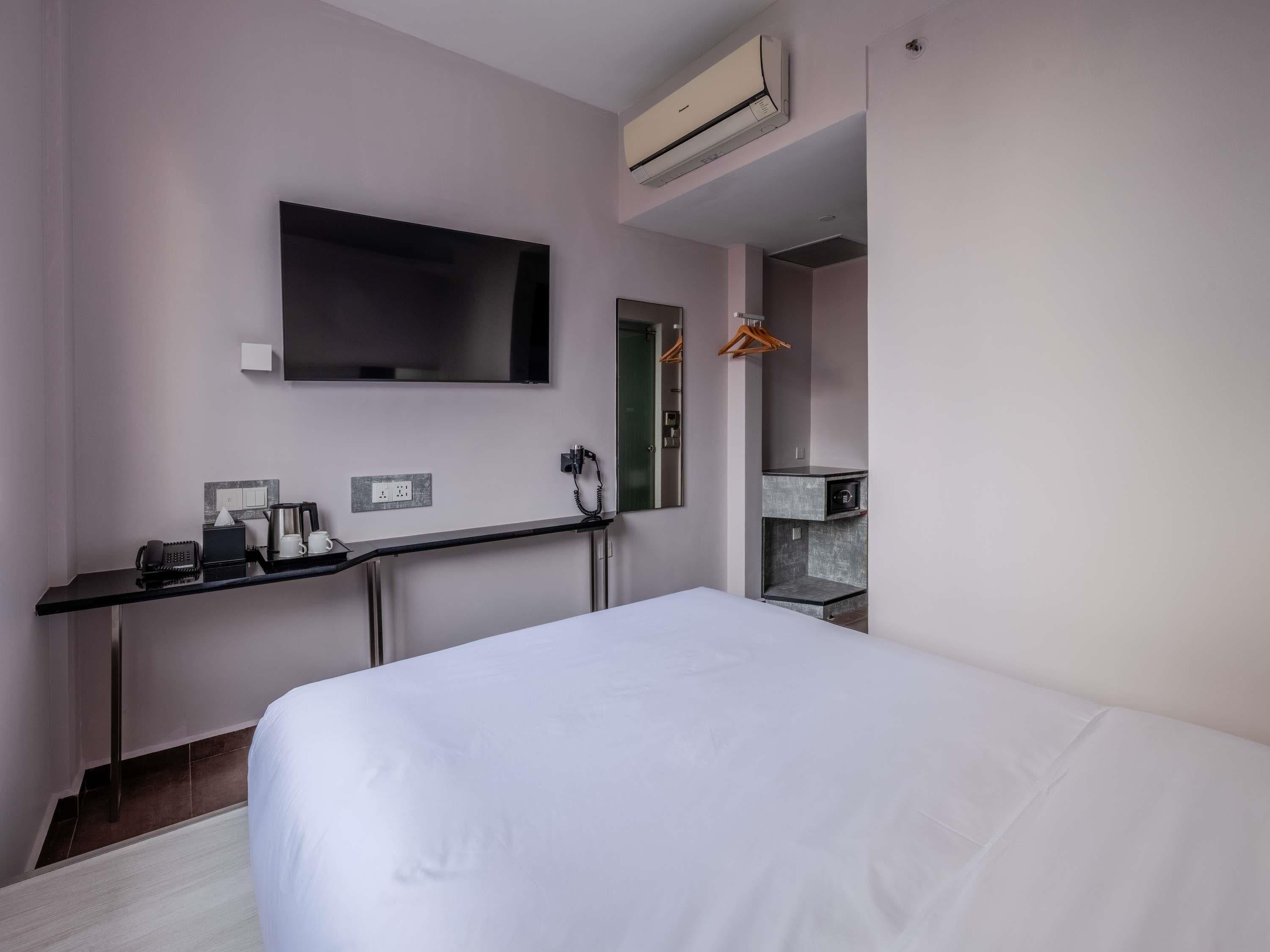 Habitación de hotel con cama, televisor de pantalla plana en la pared, escritorio con teléfono, cafetera y un mueble pequeño.