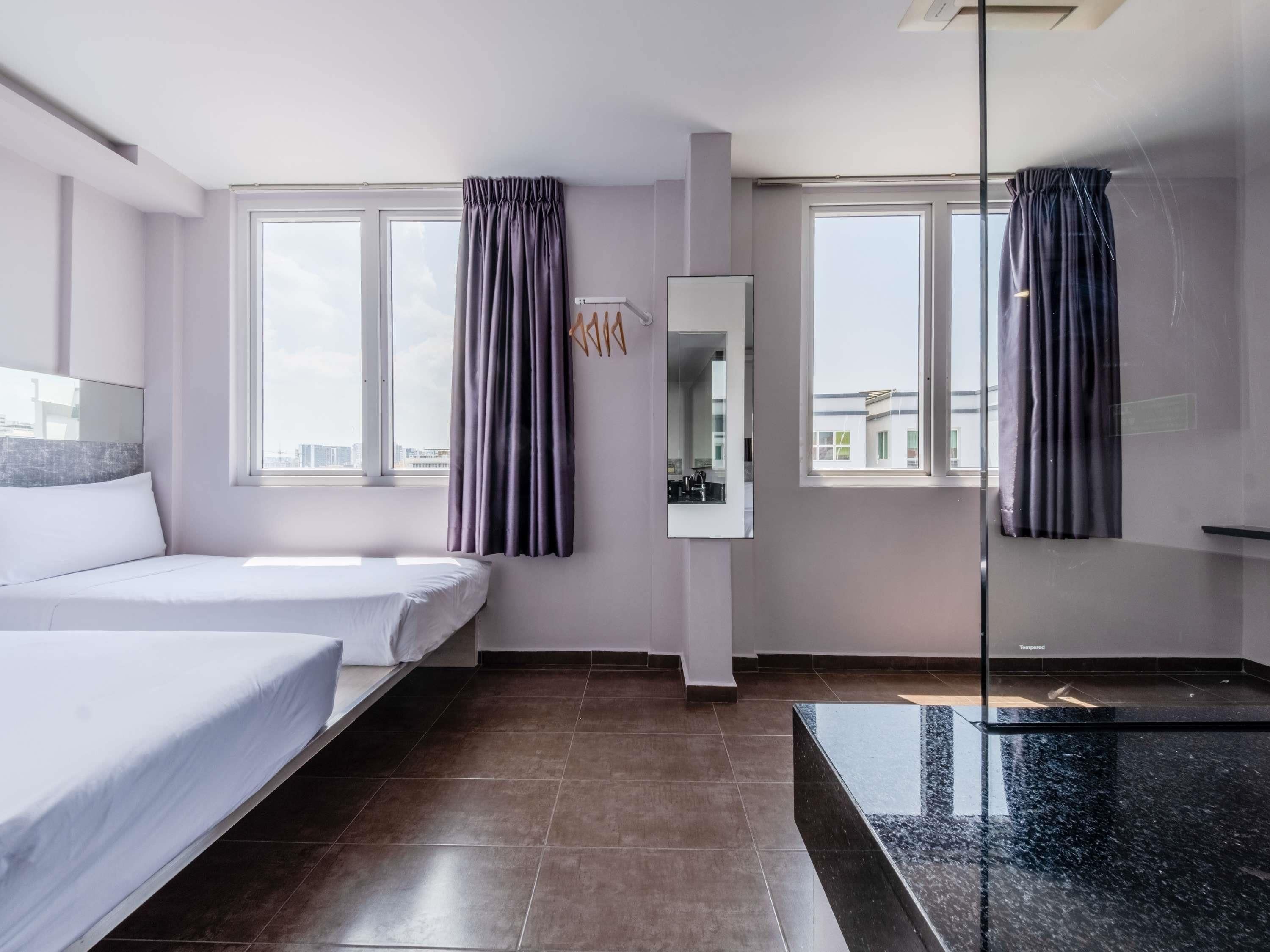 A hotel room with two beds, a large mirror, and a view of the city through the windows.