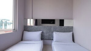 Une chambre d’hôtel avec deux lits simples, une grande fenêtre et un téléviseur fixé au mur.