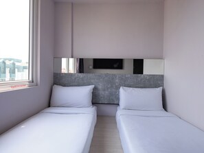 Een hotelkamer met twee enkele bedden, een groot raam en een televisie aan de muur.