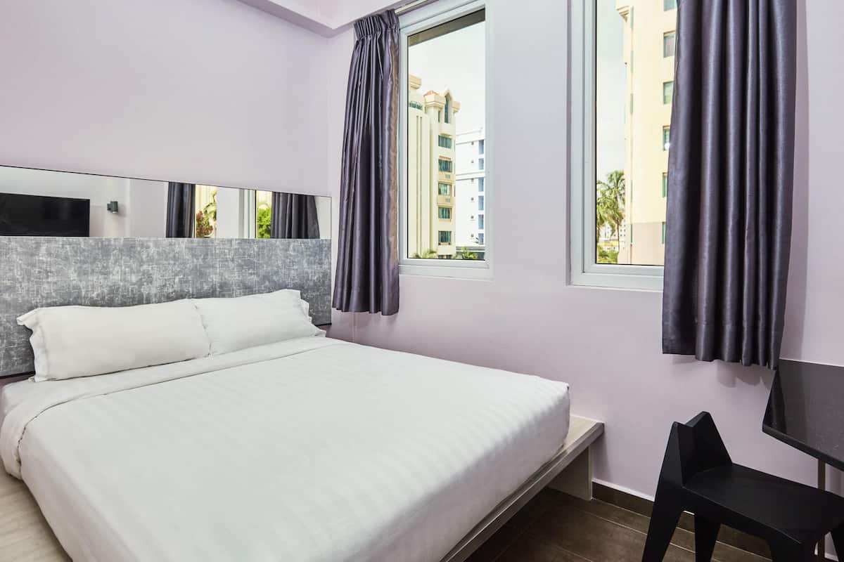 Ein modernes Hotelzimmer mit einem großen Bett, einem Schreibtisch und Blick auf Gebäude durch das Fenster.