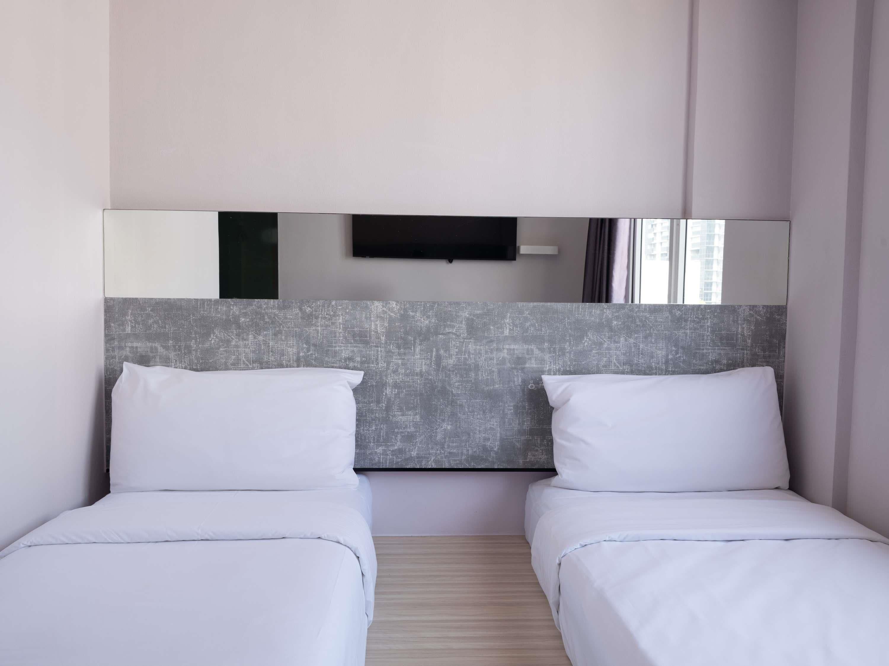 A hotel room with two beds, a large mirror, and a flat-screen TV mounted on the wall.