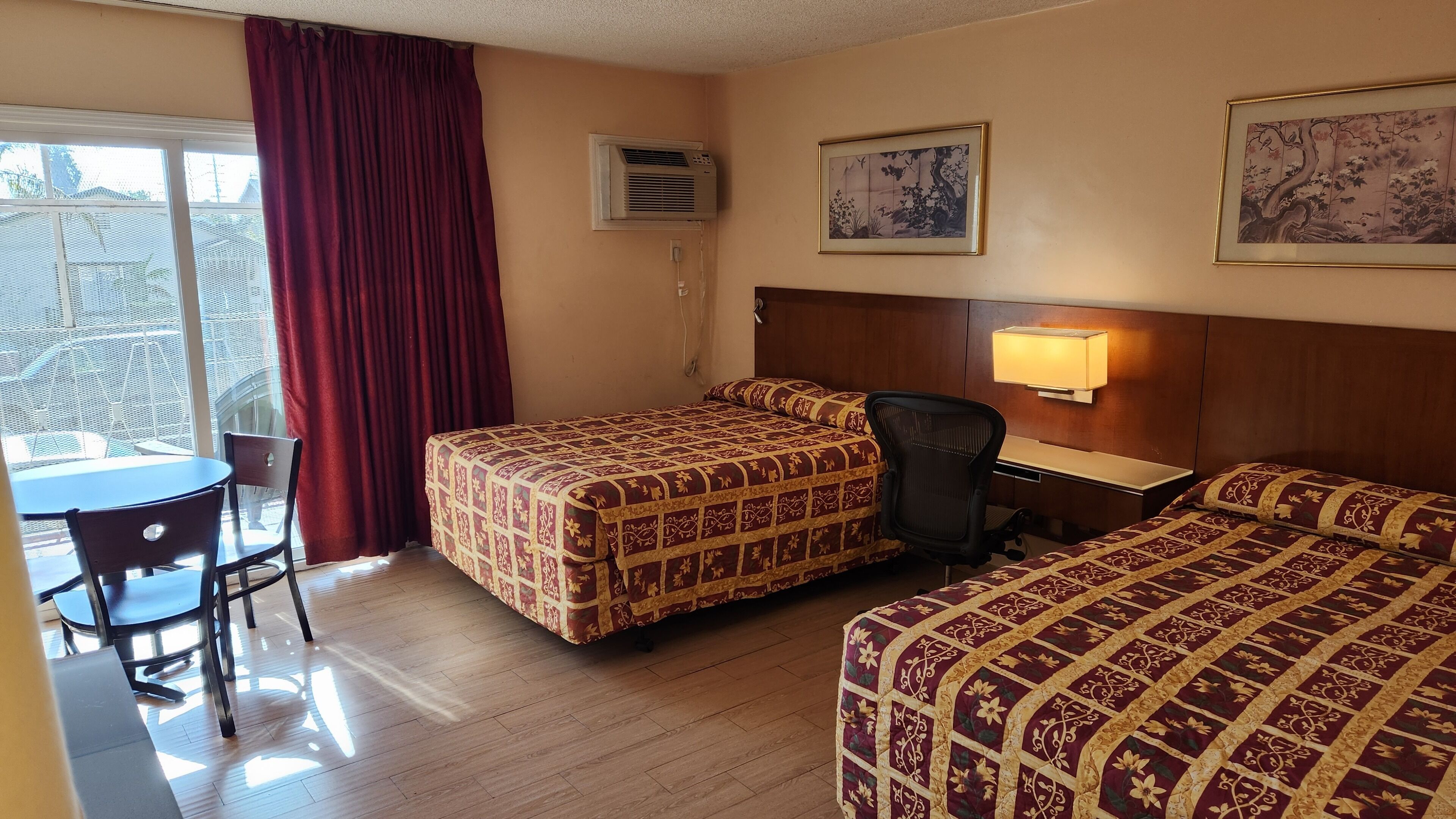 A hotel room with two beds, a desk, a chair, and a window with curtains.
