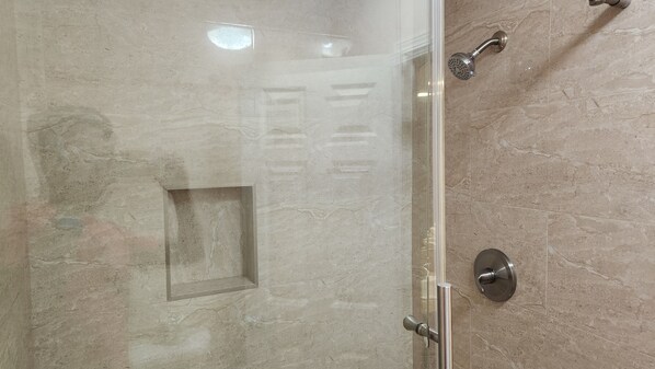A glass-enclosed shower with a handheld showerhead and a wall-mounted faucet.