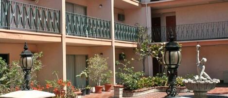 A multi-level building with balconies, potted plants, and a fountain.