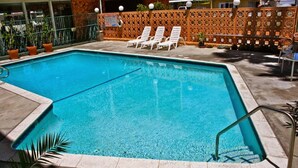 A rectangular pool with clear blue water, surrounded by a tiled deck. There are white lounge chairs and a wooden fence with decorative panels in the background.