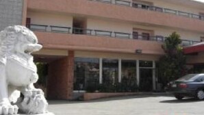 A multi-story building with a central entrance, balconies on the upper floors, and a statue in front.