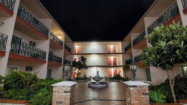 A multi-story hotel with a central courtyard featuring a fountain, brick pillars, and potted plants.