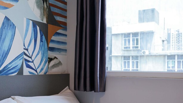 A hotel room with a bed, a window with curtains, and a wall with abstract art. - ibis budget Singapore Tulip (Singapore)