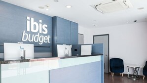 A reception desk with a sign reading 'ibis budget,' a glass partition, and two chairs. - ibis budget Singapore Tulip (Singapore)