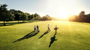 A golf course with players and a golf cart.