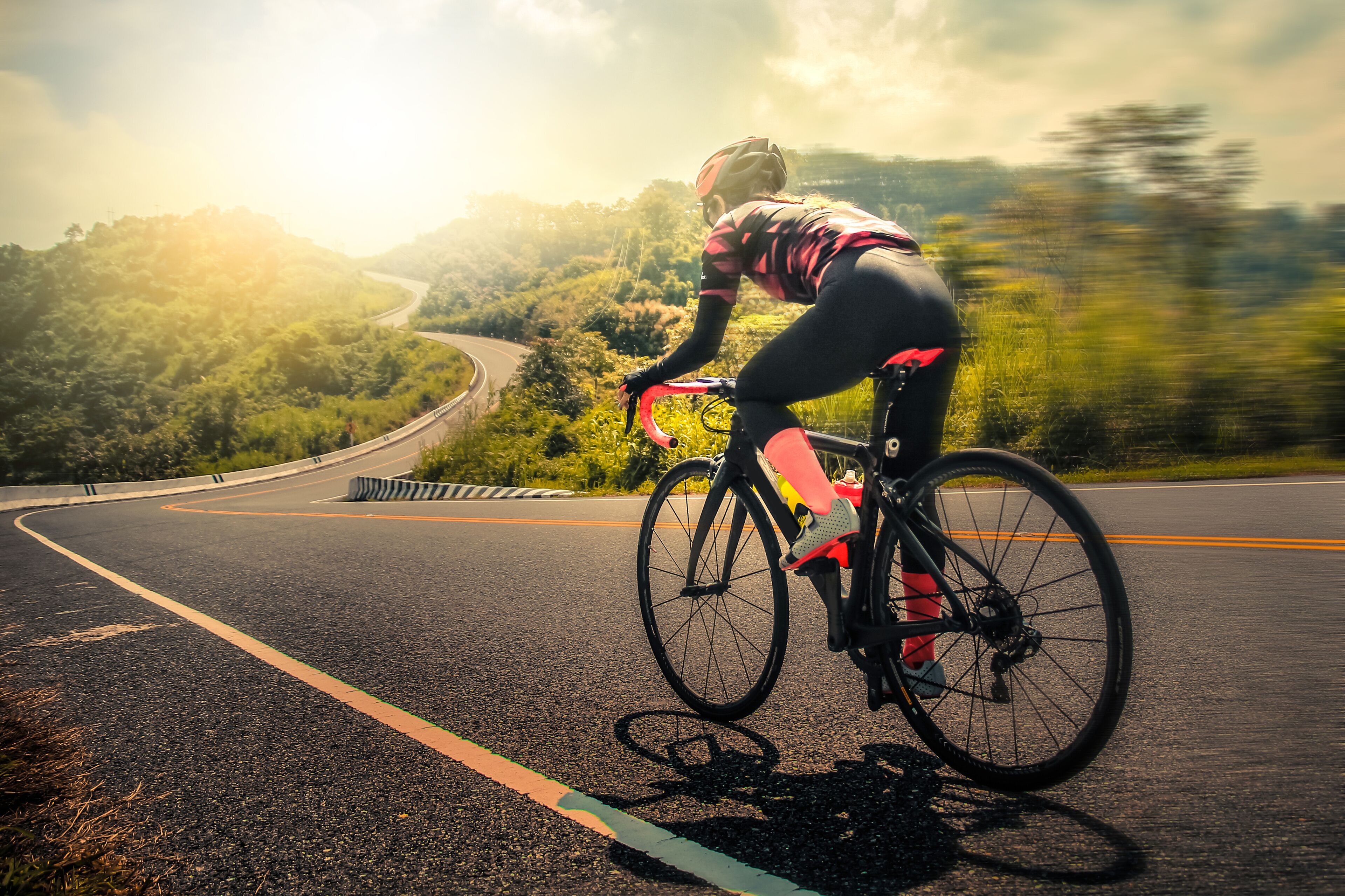 A cyclist on a road with a scenic view of a winding road and greenery in the background.