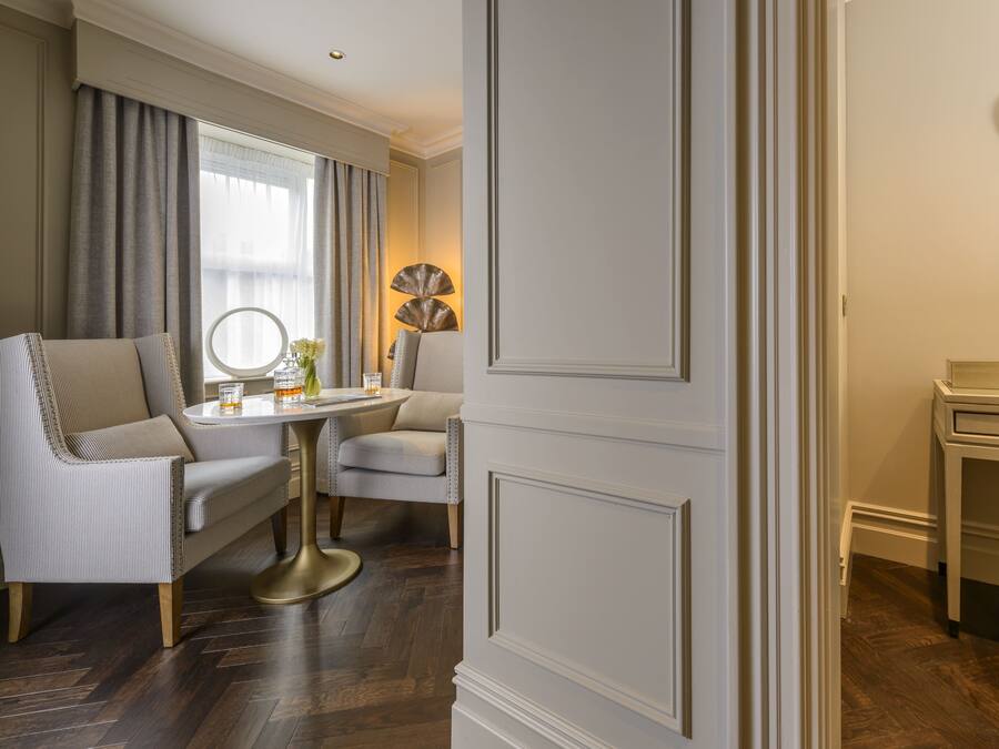 A room with a round table, two chairs, a mirror, and a small side table with a lamp.