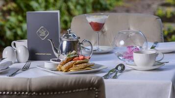 A breakfast setting with a menu, a teapot, a martini glass, and a cup on a table.