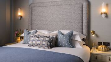 A neatly made bed with a grey headboard, multiple pillows, bedside lamps, and a small bedside table with a bottle and a decorative item.