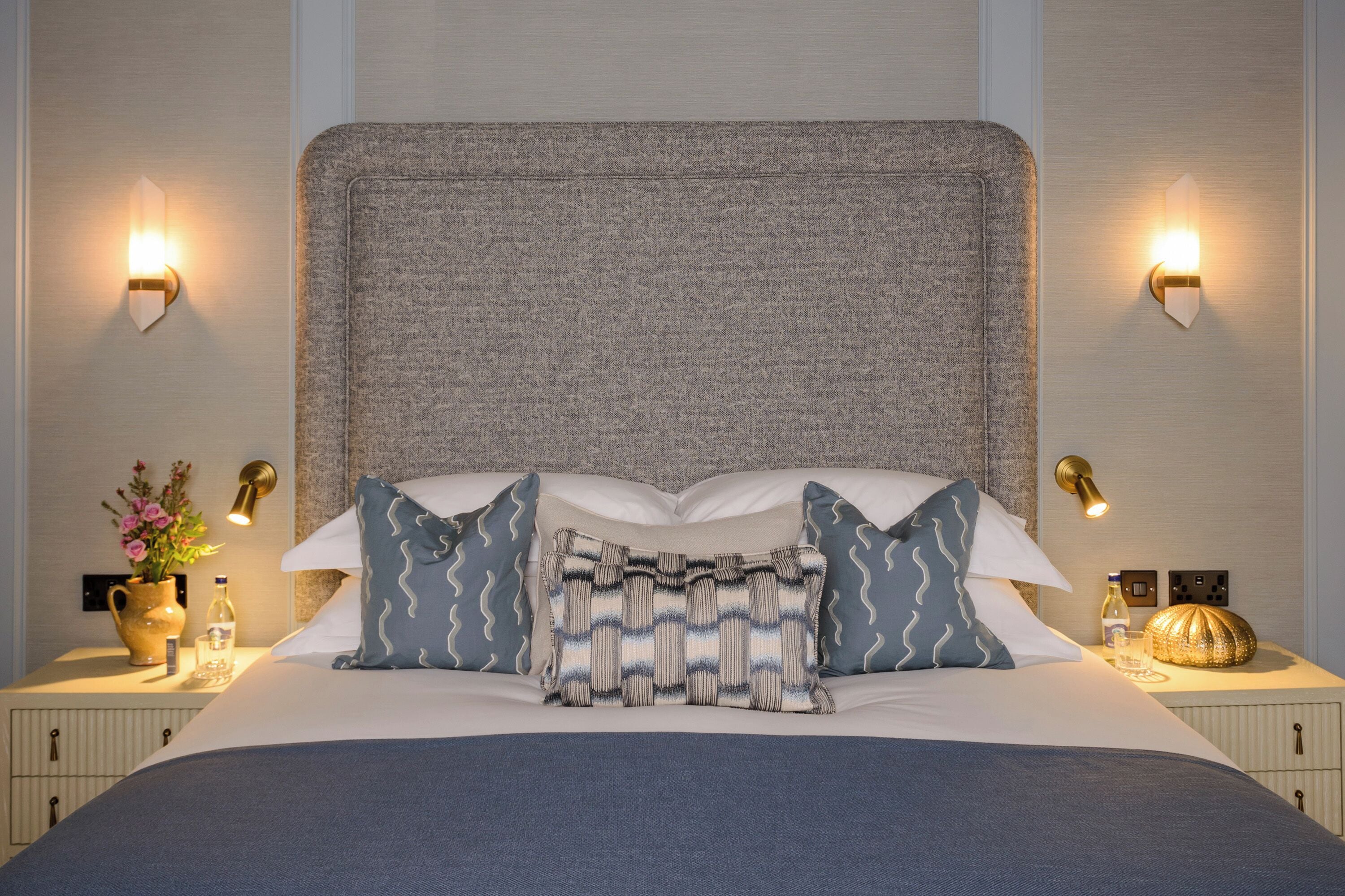 A hotel room with a large bed, two bedside lamps, a vase with flowers, and a decorative item on the nightstand.