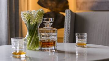 A round table with a crystal decanter, a glass vase with flowers, and two glasses of amber liquid.