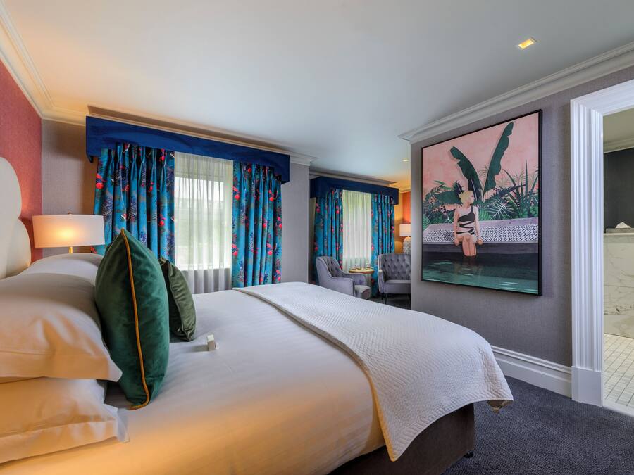 Habitación de hotel con una cama grande, dos mesitas de noche, una silla y un cuadro en la pared.