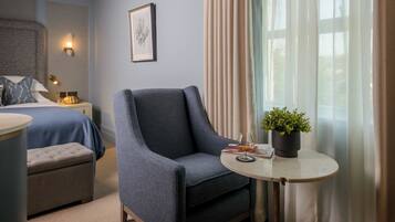 Habitación de hotel con una cama, una silla, una mesita con una planta y una ventana con cortinas.