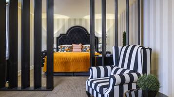 Habitación de hotel con cama, un sillón a rayas, una mesita y una planta en maceta.