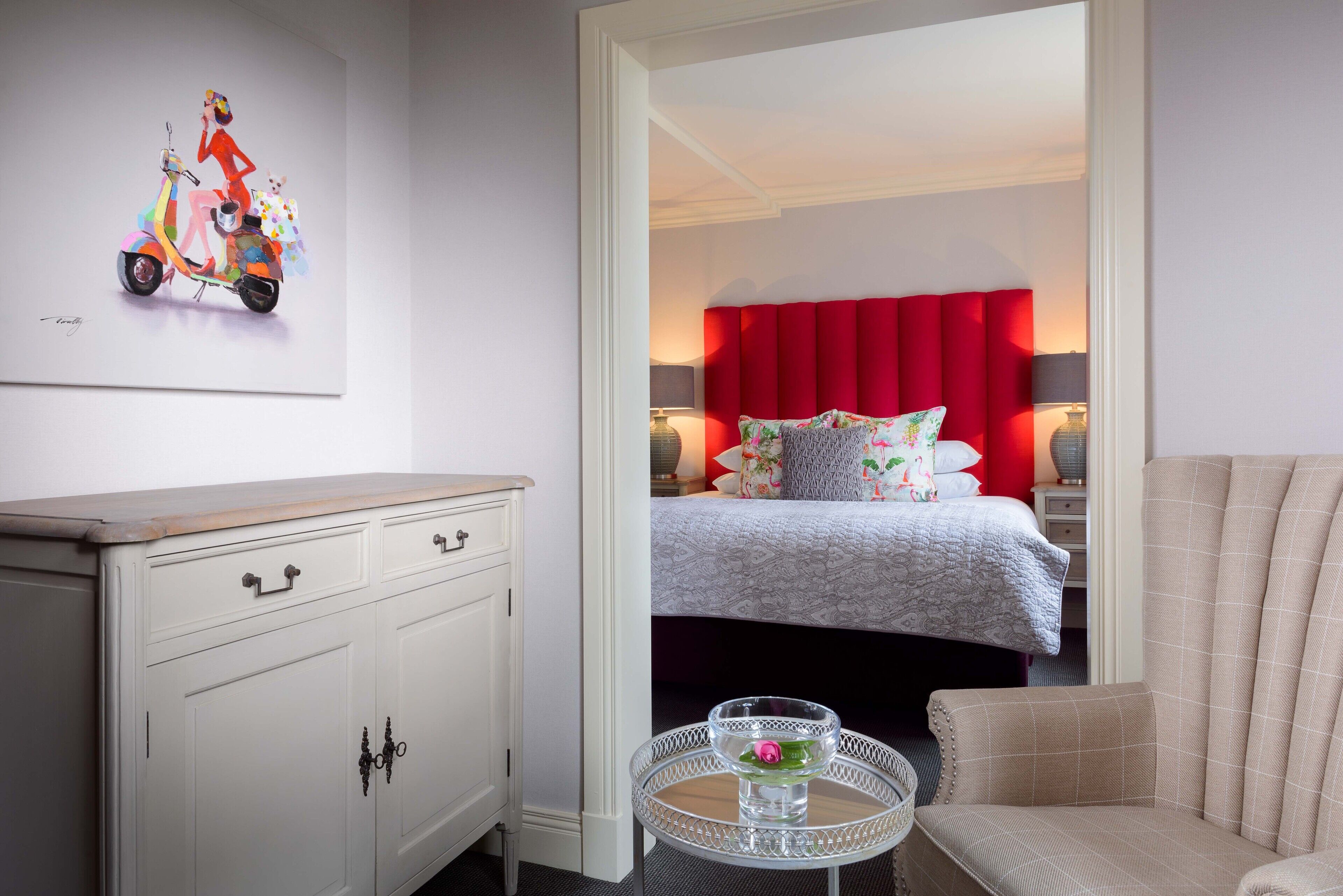 Une chambre d’hôtel avec un lit, une commode blanche, une table ronde avec un plateau en verre et un rideau rouge.