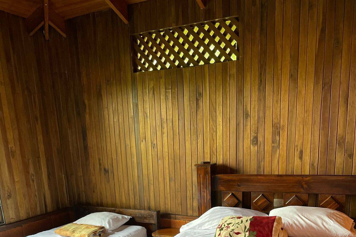 A room with two single beds, wooden walls, and a slatted ceiling.