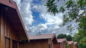 Une rangée de cabanes en bois, reliées par un chemin de gravier, et entourées de verdure.