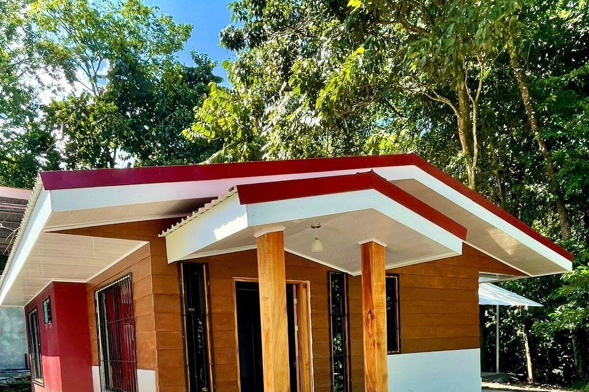A modern single-story house with a red roof, wooden pillars, and a gravel driveway.