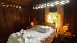 Une pièce aux murs lambrissés, avec un lit, deux lampes de chevet et une fenêtre avec des rideaux.