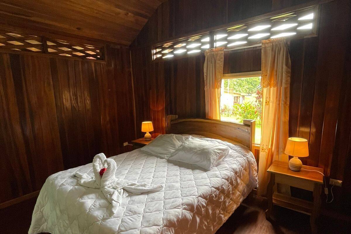 A wooden-paneled room with a bed, two bedside lamps, and a window with curtains.