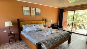 Une chambre spacieuse avec un grand lit, deux tables de chevet et un balcon avec vue.