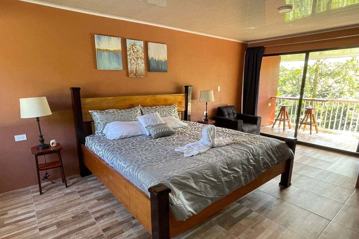 A spacious bedroom with a large bed, two bedside tables, and a balcony with a view.