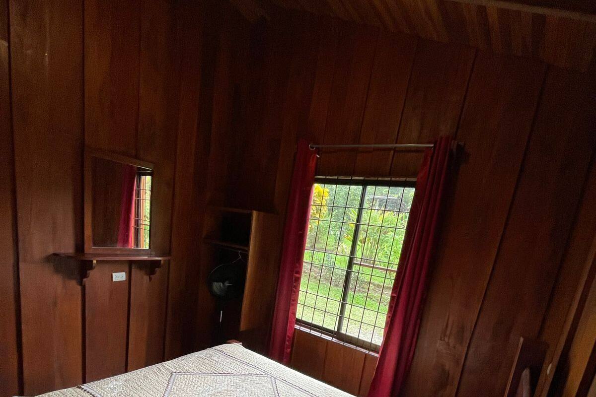 A wooden room with a bed, a small window, and a mirror on the wall.