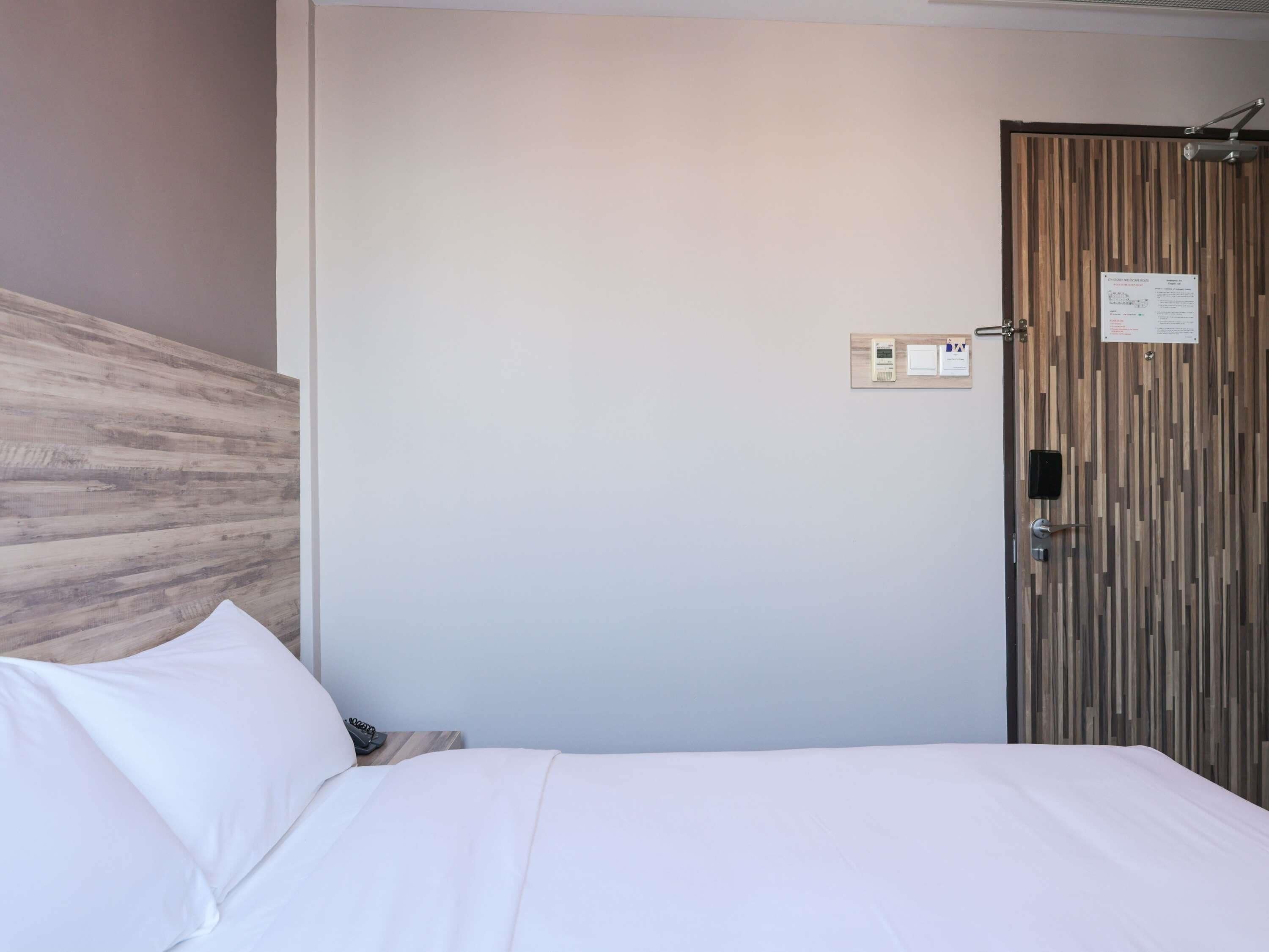 Et hotelværelse med en seng, en træsenggavl, en dør med lås og en vægmonteret lampe.