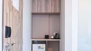 Una kitchenette compacta con refrigerador integrado, cafetera y un estante pequeño.
