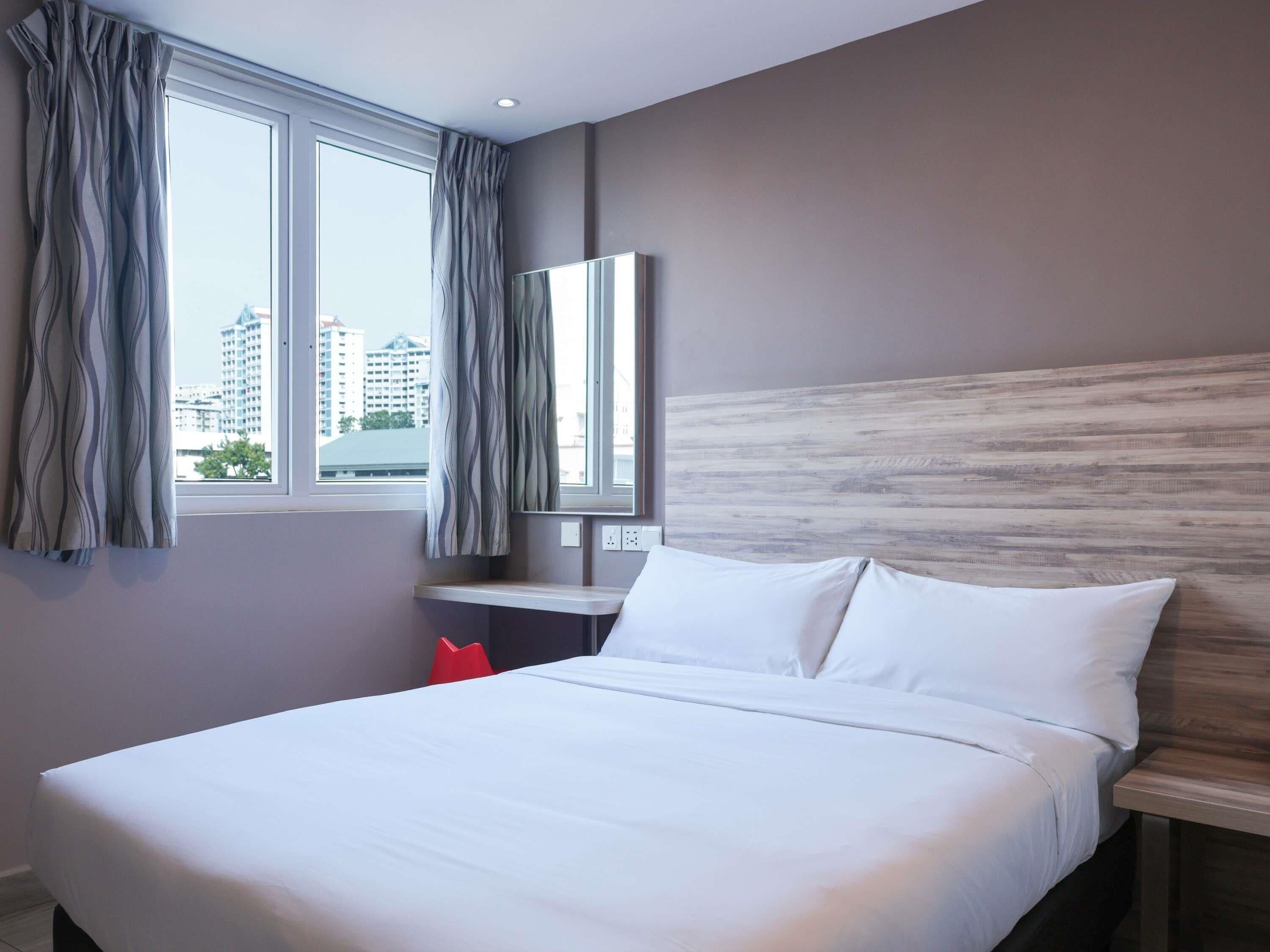 A hotel room with a bed, a nightstand, a mirror, and a window with curtains.