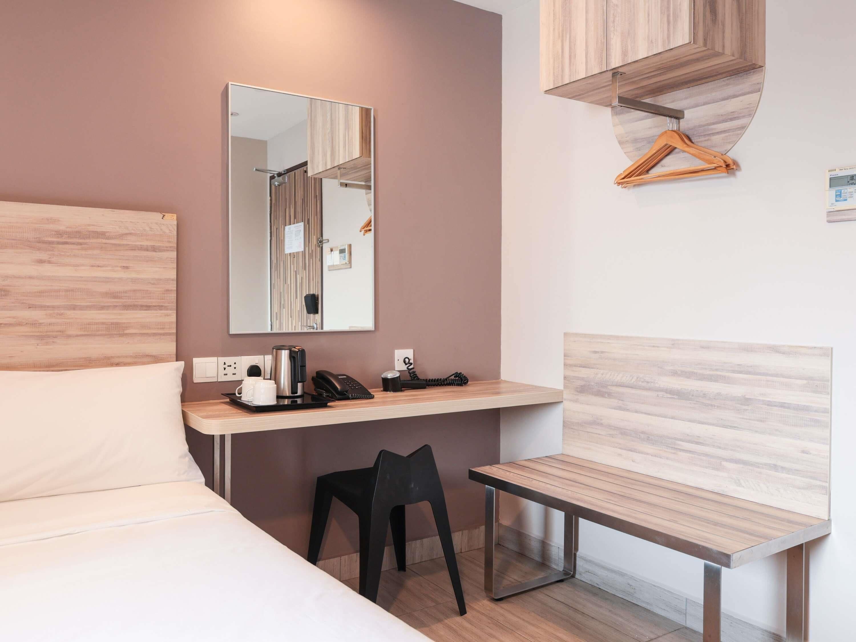 A modern hotel room with a bed, a desk with a telephone, a coffee maker, and a chair.