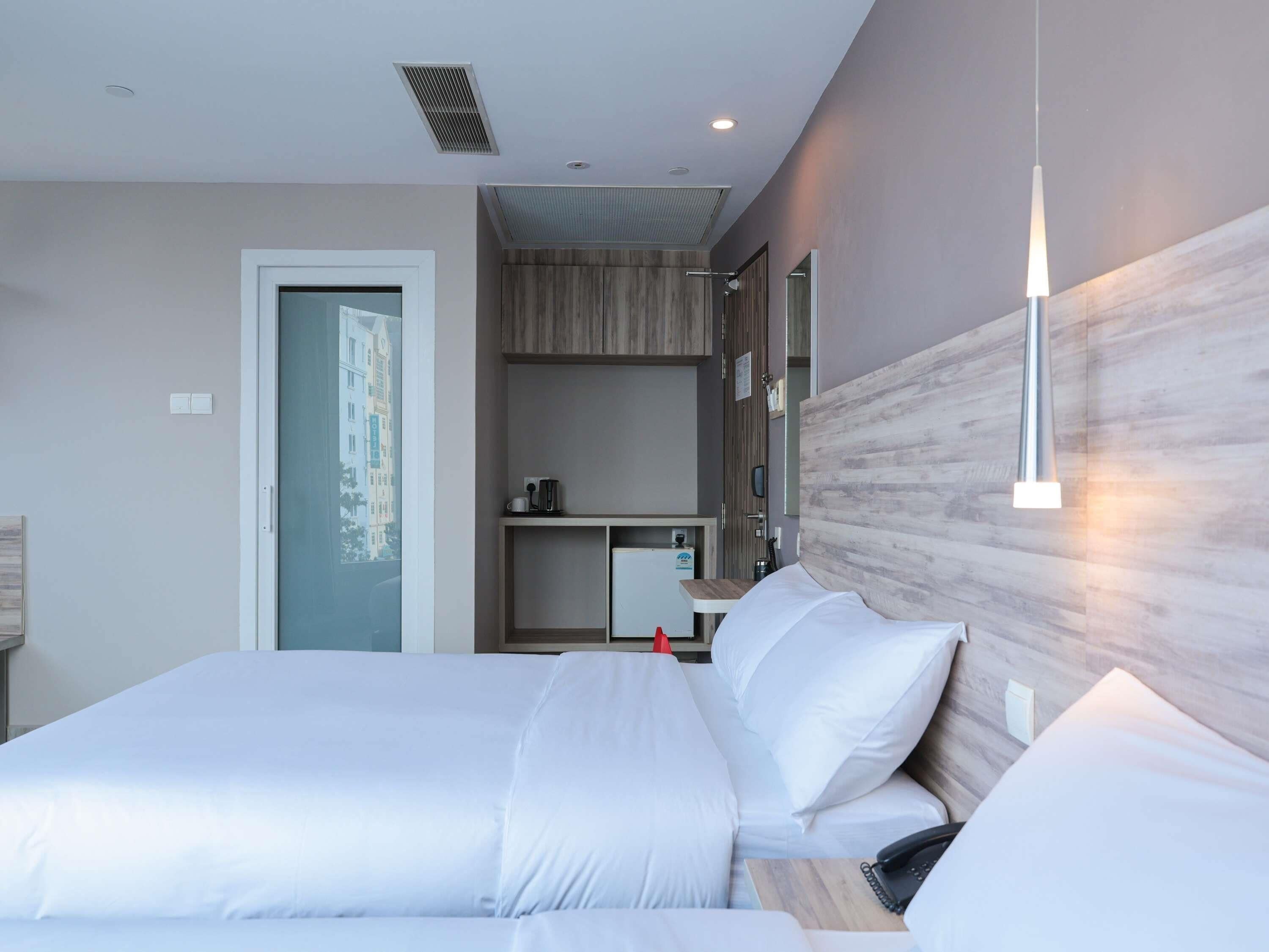 Une chambre d’hôtel moderne, dotée d’un grand lit, d’un bureau, d’un miroir et offrant une vue sur les bâtiments à travers la fenêtre.